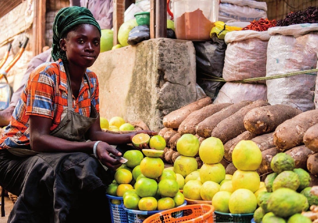 A young trader cuts citrus fruit at her stall of oranges and yams.
